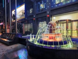 Un hotel moderno con una fuente central, entrada de cristal y un cartel.