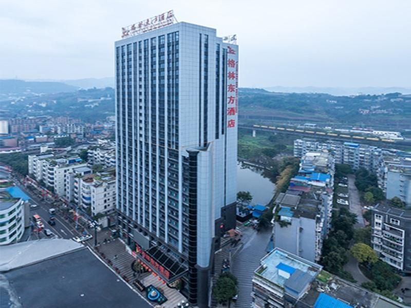 A high-rise hotel with a modern glass facade, located in an urban setting with surrounding buildings and a river.
