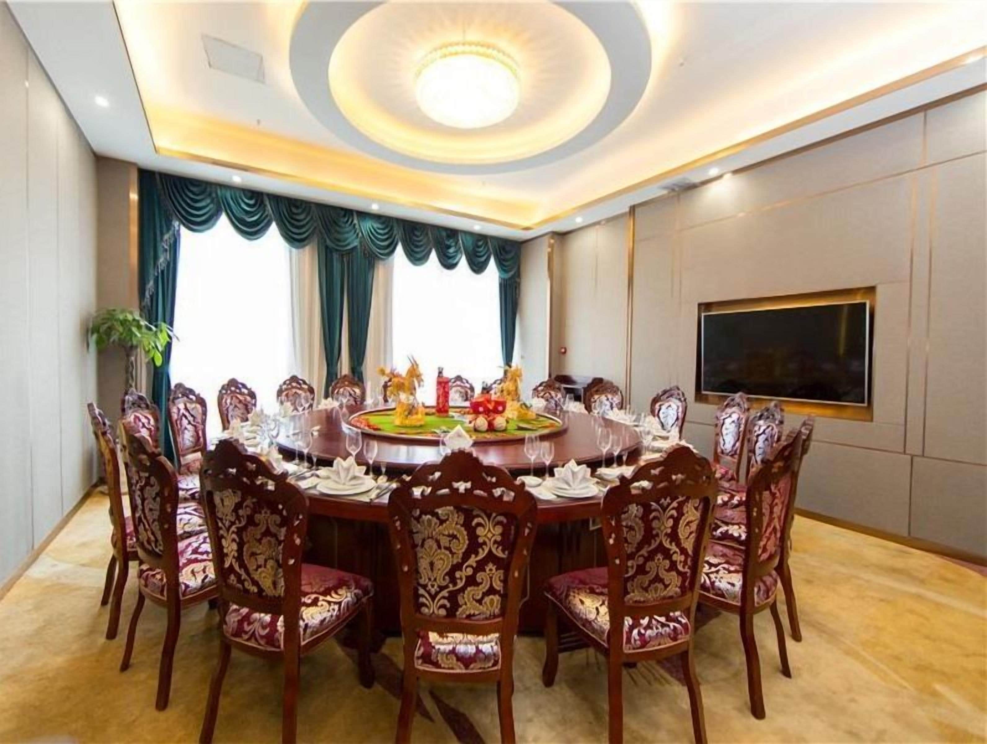 A conference room with a round table, ornate chairs, a chandelier, and a large window with curtains.