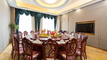 A conference room with a round table, ornate chairs, a chandelier, and a large window with curtains.