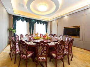 Un salón de conferencias con una mesa redonda, sillas ornamentadas, una araña y un amplio ventanal con cortinas.