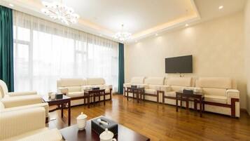 A spacious living room with a large sofa set, a coffee table, and a flat-screen TV mounted on the wall.