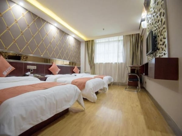 A hotel room with three beds, a TV, a desk, and a window with curtains.