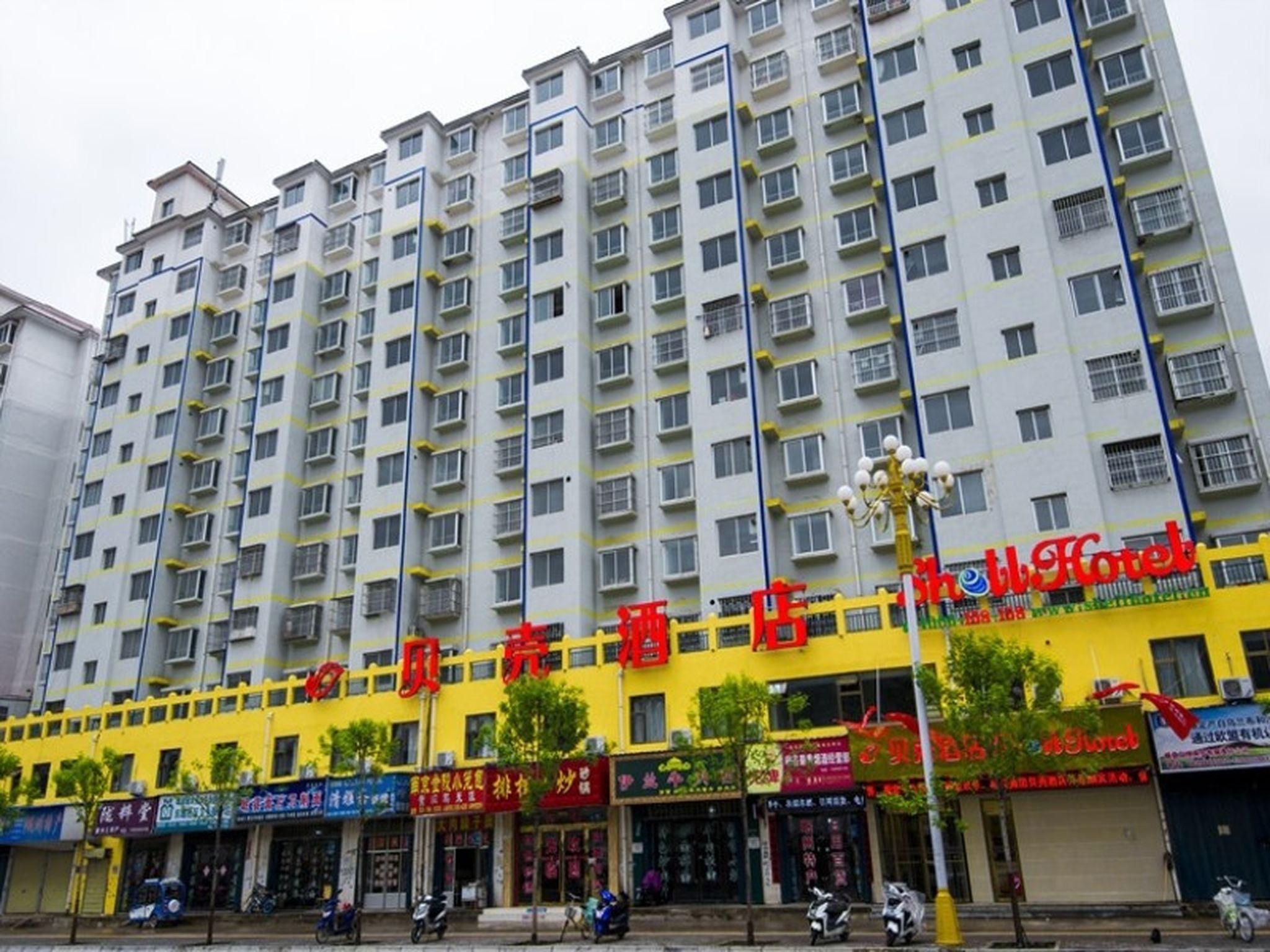 A multi-story hotel with a yellow facade, multiple balconies, and various storefronts at the ground level.