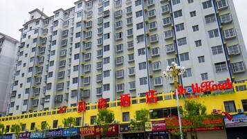 A multi-story hotel with a yellow facade, multiple balconies, and various storefronts at the ground level.