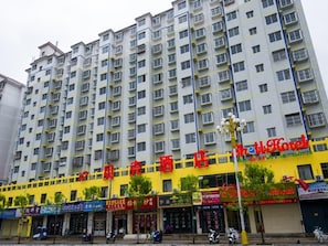 A multi-story hotel with a yellow facade, multiple balconies, and various storefronts at the ground level.