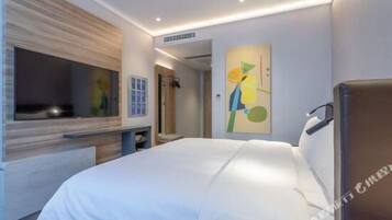 A modern hotel room with a large bed, a flat-screen TV mounted on the wall, a painting on the wall, and a wooden headboard.