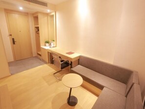 A room with a wooden floor, a grey sofa, a small round table, a desk with a chair, and a wardrobe. - Shell Hotel Chuzhou Economic Development Zone Internation Shangcheng (Chuzhou)
