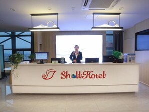 A reception desk at Show Hotel with a large screen, two monitors, and a plant. - Shell Hotel Chuzhou Economic Development Zone Internation Shangcheng (Chuzhou)