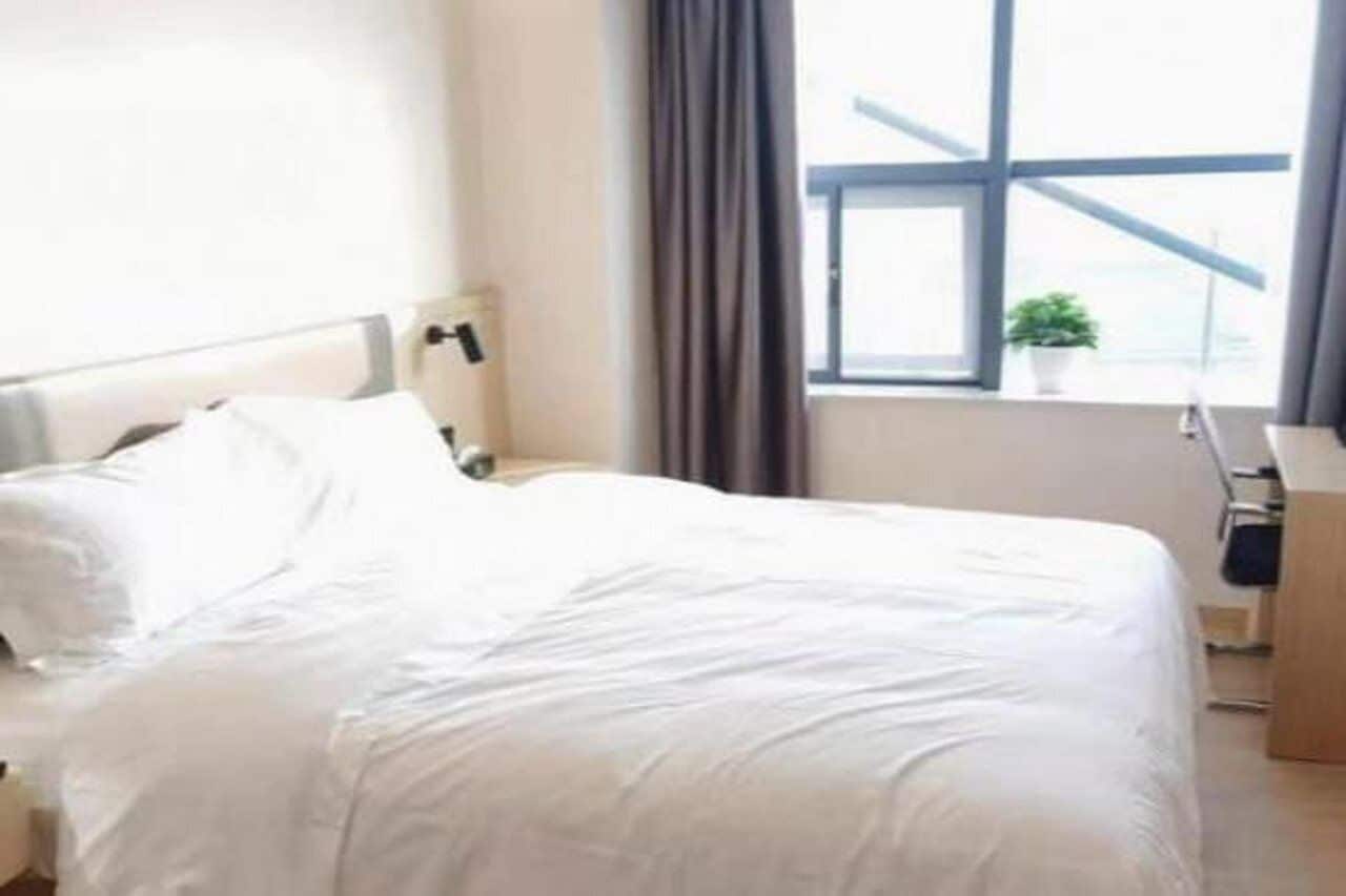 Une chambre d’hôtel avec un lit, une table de chevet, une lampe, une fenêtre avec des rideaux et une vue sur le ciel.