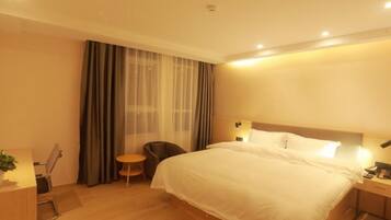 A hotel room with a bed, bedside table, lamp, chair, and a small table with a plant.