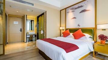 Une chambre d’hôtel avec un grand lit, une table de chevet avec une lampe, une œuvre d’art accrochée au mur et une salle de bain visible à travers une porte ouverte.