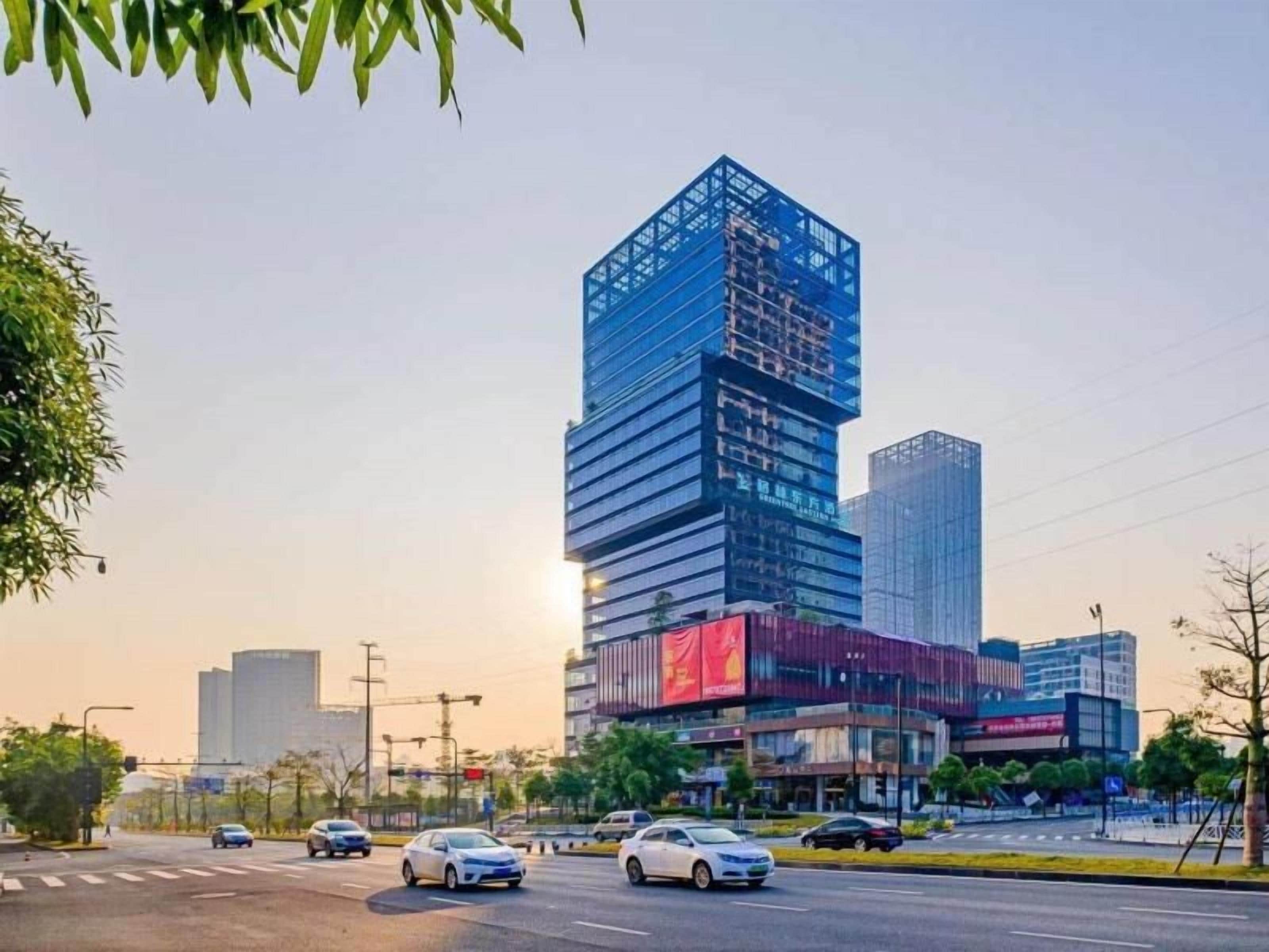 A modern urban street with a prominent multi-story building featuring a glass facade and a red advertisement banner.