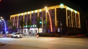 Un hotel con una fachada moderna, iluminado por luces cálidas, que presenta una entrada destacada y una vista despejada de la calle.