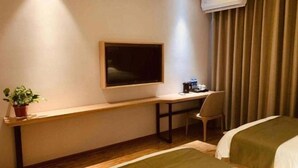 Habitació d'hotel amb llit, escriptori, cadira, planta en test i finestra amb cortina.