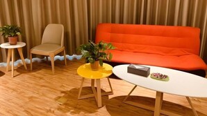 Una habitación con una silla color beige, un taburete amarillo, una mesa blanca y un sofá naranja.