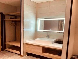 Un baño con un lavamanos blanco, un espejo con luz y estantes de madera.