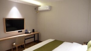 Una habitación de hotel con una cama, un escritorio con una silla, un televisor y un equipo de aire acondicionado.