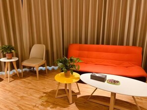 A room with a beige chair, a yellow stool, a white table, and an orange sofa.