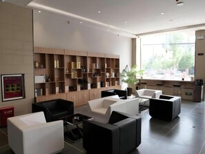 A modern lobby with a seating area, a bookshelf, and a view of the outside.