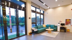 A modern lobby with a green sofa, a round wooden coffee table, and a desk with a computer.