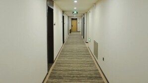 A hotel hallway with carpeted floors, doors on both sides, and a green exit sign on the ceiling.
