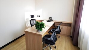 Ein Konferenzraum mit einem Holztisch, zwei schwarzen Bürost ühlen, einem Topf mit Pflanze und einer Kaffeemaschine.