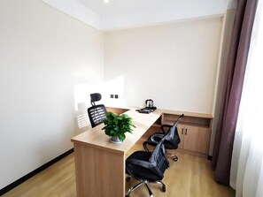 Un salón de conferencias con una mesa de madera, dos sillas de oficina negras, una planta en maceta y una cafetera.