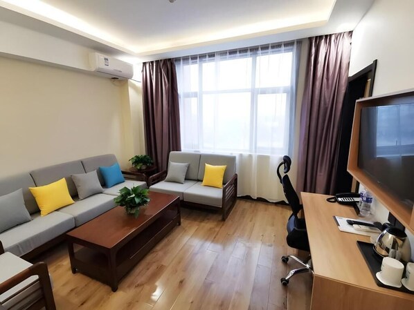 A modern living room with a sofa set, a wooden coffee table, a desk with a computer, and a television.