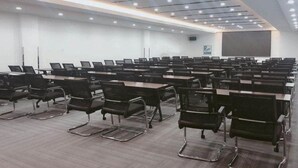 Un salón de conferencias con mesas y sillas dispuestas en filas, una pantalla grande y un proyector.