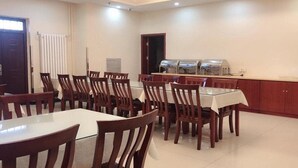 Una sala de conferencias con una larga mesa, varias sillas, una zona de bufé con dispensadores de alimentos y una puerta.