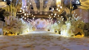 Un espacio interior con escenario, arreglos florales e iluminación colgante.