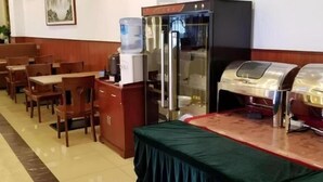 Un comedor con mesas y sillas de madera, un dispensador de agua, un refrigerador y una estación de buffet.