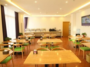 Un espace repas avec plusieurs tables et chaises, un coin cuisine équipé d’appareils électroménagers et une grande fenêtre avec des rideaux.