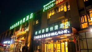 Un hotel con señalización iluminada en verde y amarillo, que muestra información de contacto y tarifas de habitaciones.