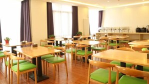 Un espace repas comprenant plusieurs tables et chaises, un comptoir où sont présentés des aliments, et une fenêtre avec des rideaux.