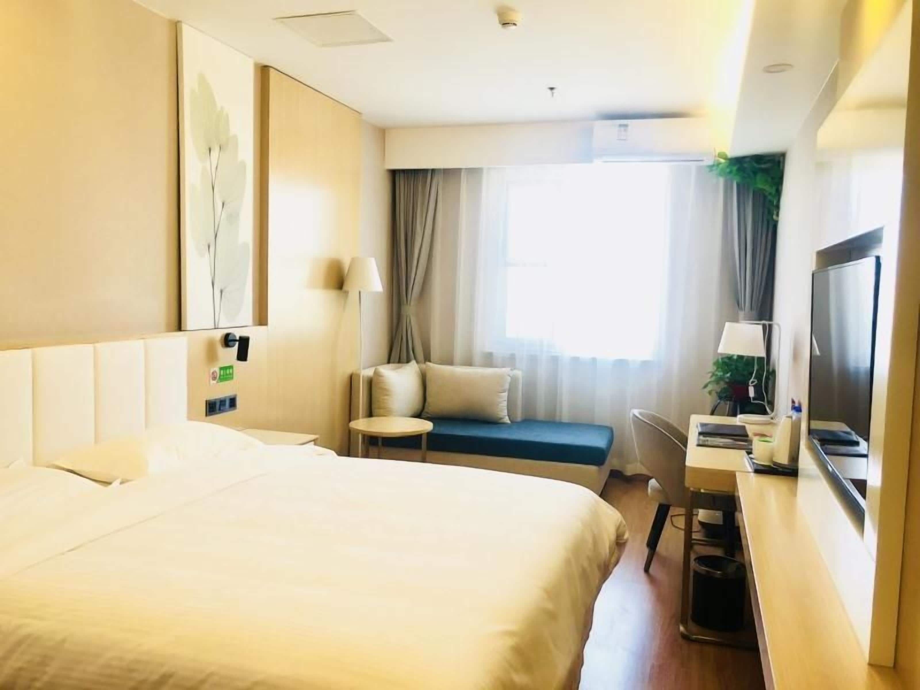 A hotel room with a bed, a desk, a chair, a TV, and a window with curtains.