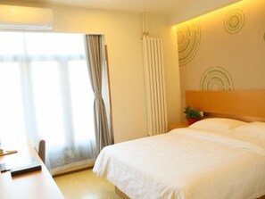 Hotellihuone, jossa on sänky, työpöytä, ikkuna verhoilla ja seinä, jossa on pyöreä kuvio.