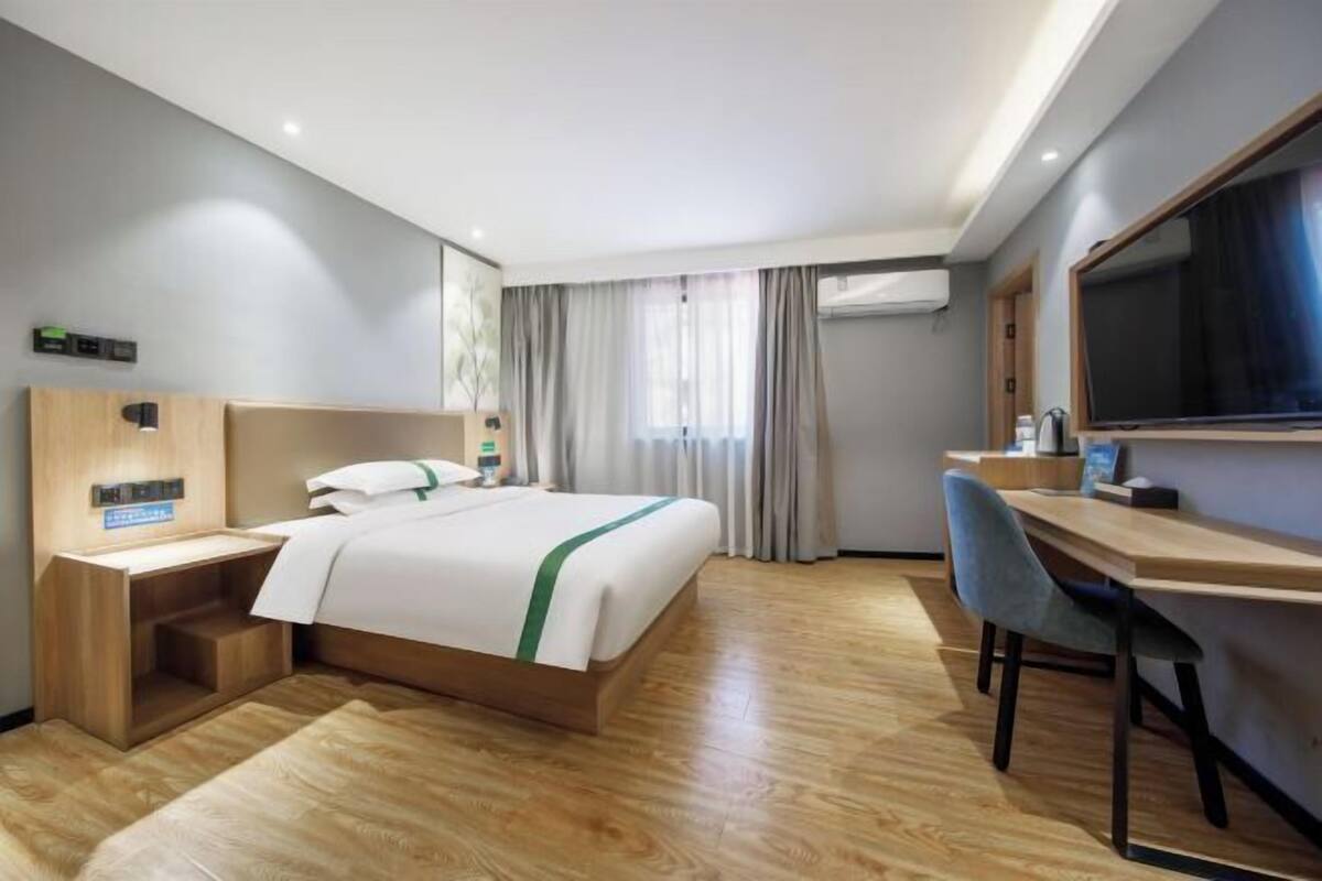 A hotel room with a bed, desk, chair, and a television.