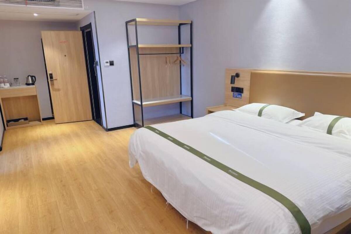 A hotel room with a bed, a wooden desk, a wardrobe, and a shelf unit.