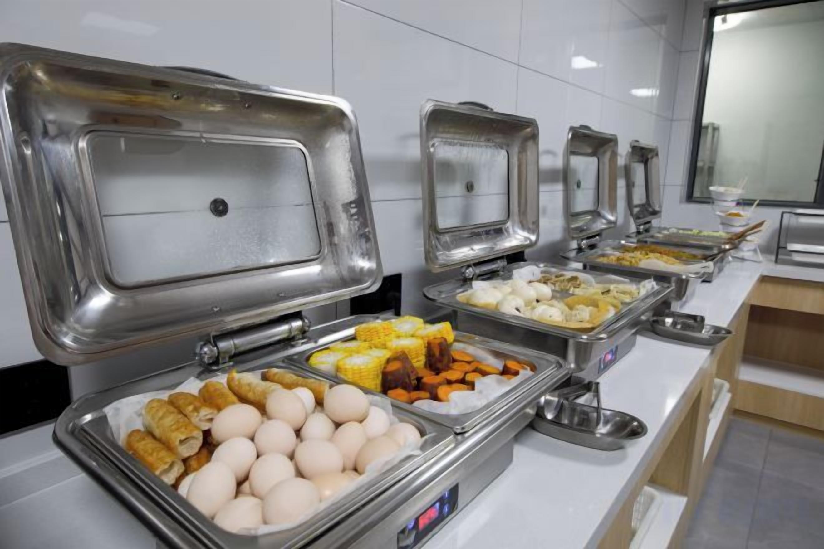 A buffet with various food items in metal containers, a stainless steel counter, and a tiled wall.