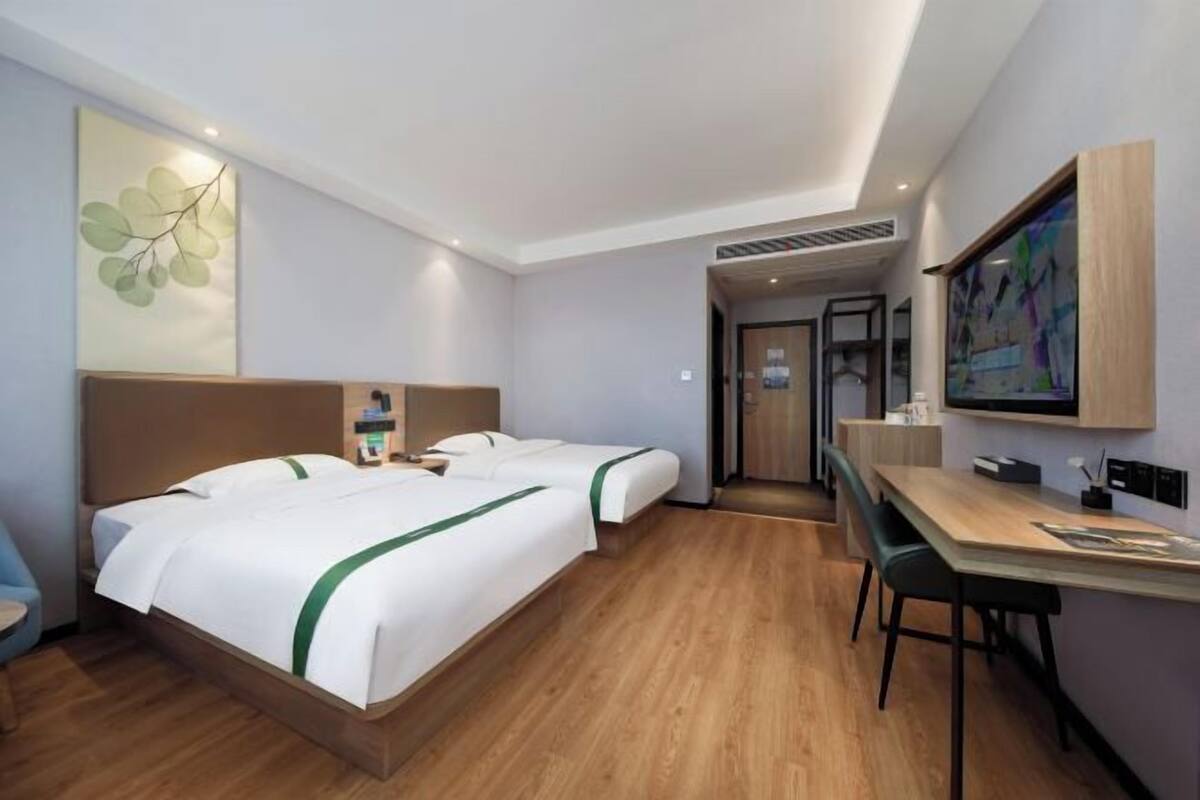 A hotel room with two beds, a desk, and a chair. There is a television on the wall and a door leading to another room.