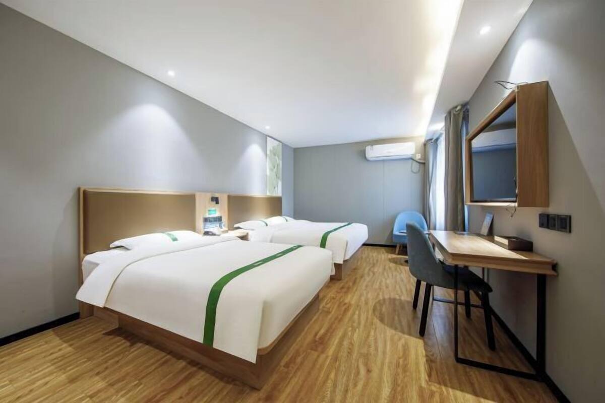 A hotel room with two beds, a desk, a chair, and a mirror.