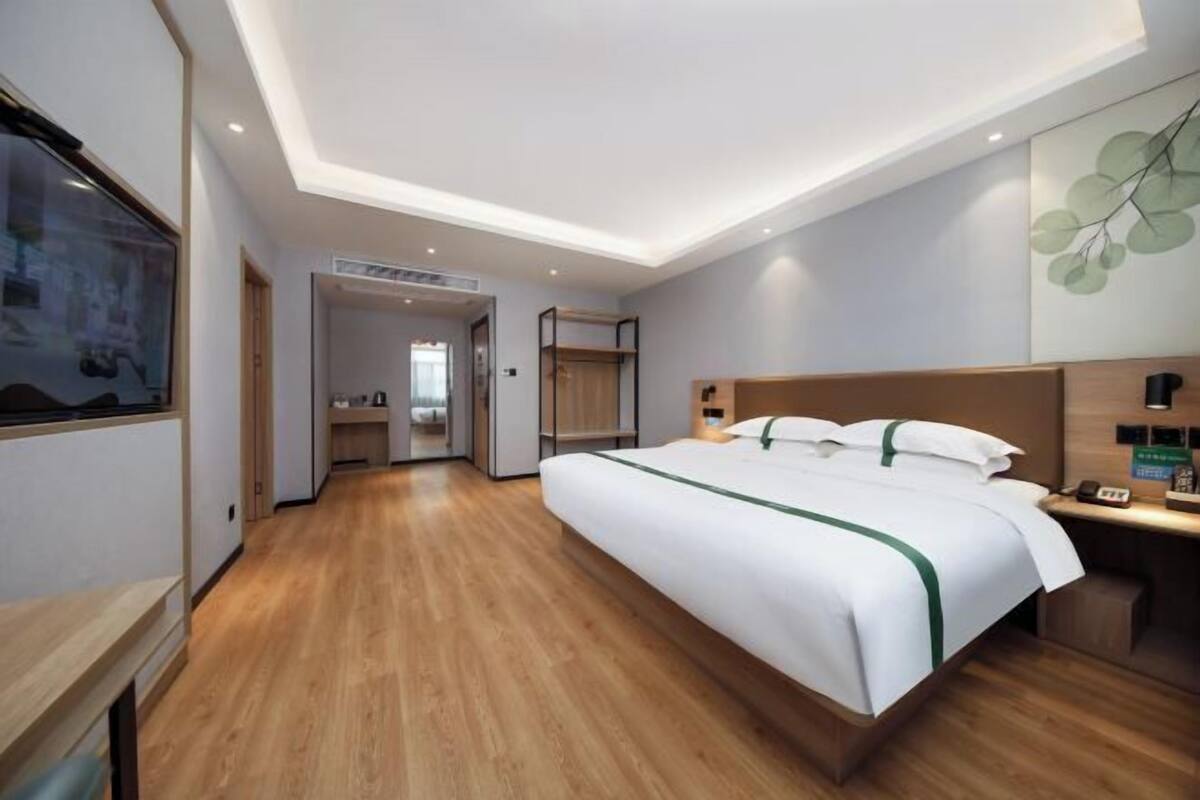 A modern hotel room with a large bed, wooden flooring, a built-in wardrobe, and a small desk with a telephone.