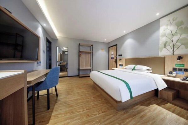 A hotel room with a bed, desk, chair, and a large mirror.