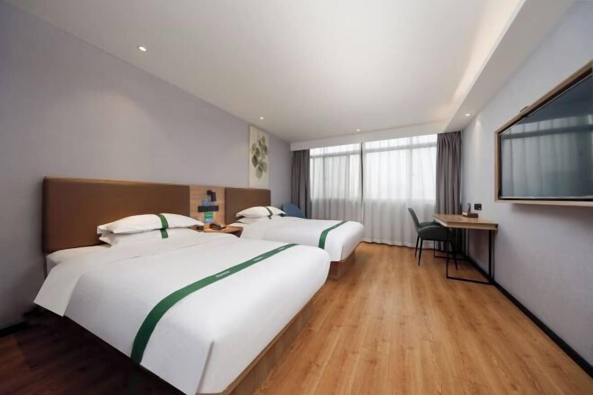 A hotel room with two beds, a desk, and a large window.