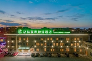 Um hotel com placa verde, vários andares e estacionamento.