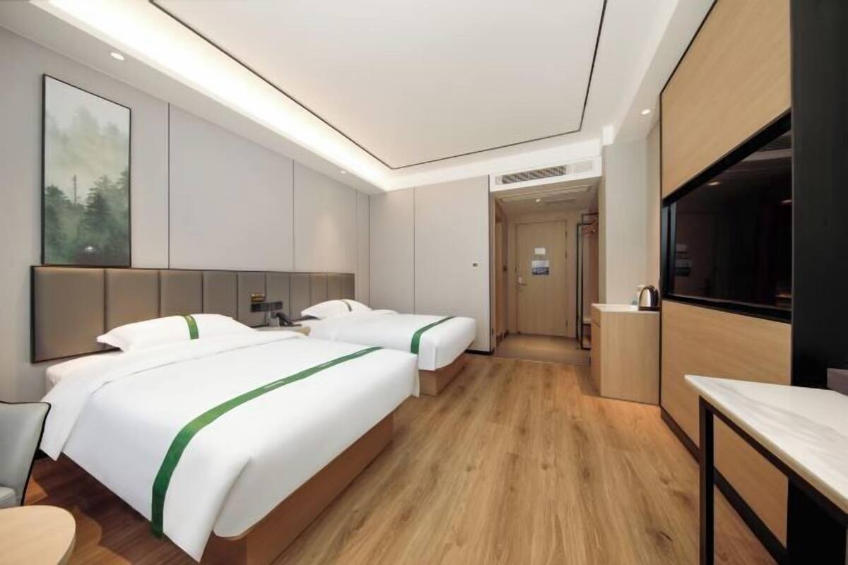 A hotel room with two beds, a TV, a desk, and a painting on the wall.