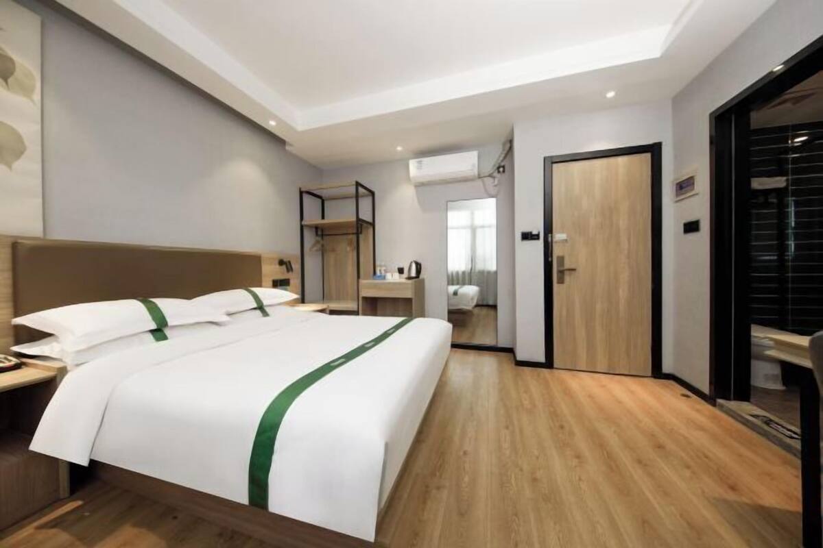 A modern hotel room with a large bed, wooden flooring, a built-in wardrobe, and a separate bathroom.
