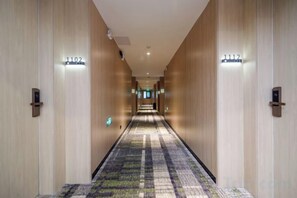 Un pasillo de hotel con piso alfombrado, paredes de madera y puertas numeradas.